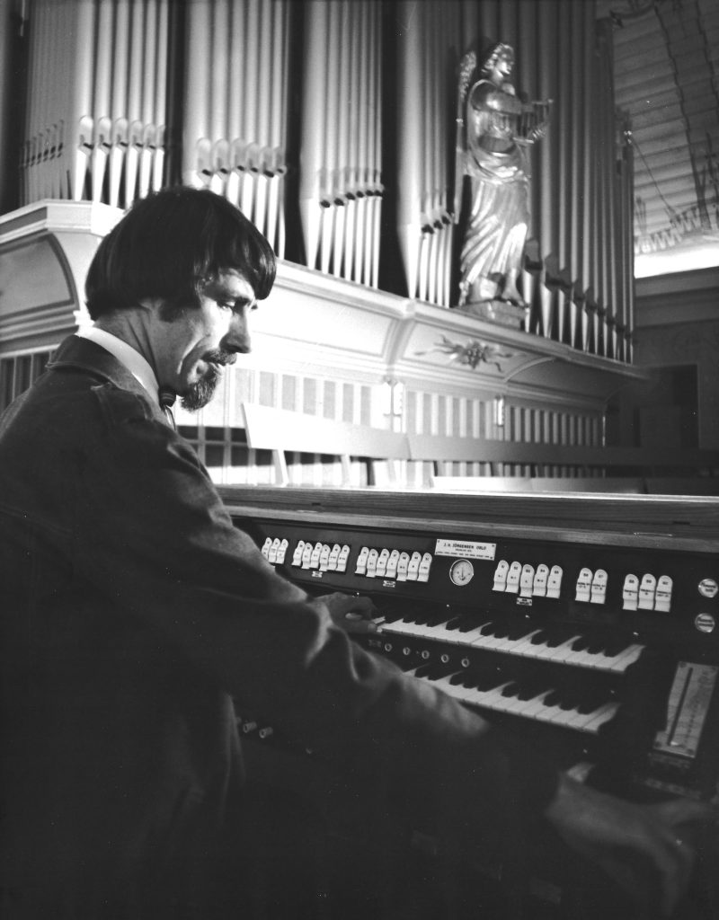 Egil Hovland med halvlangt hår og skjedd spiller orgel i Glemmen kirke.